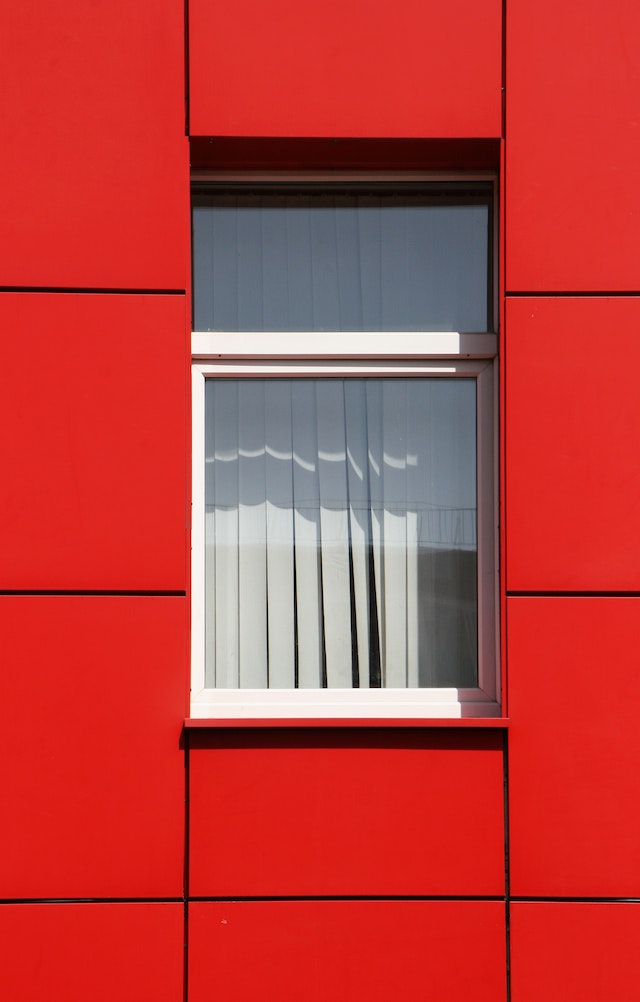 Exterior of a red tiled building with a window in the center covered with white blinds.